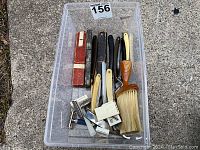 Entire lot showing all items in a clear plastic bin on pavement including razors, cases, brush, and blades.