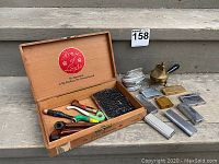 Overall view of the wooden box containing smoking pipes and surrounding lighters and container.