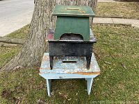Three old wooden stools stacked outdoors against a large tree, showing color, paint wear, and size differences.