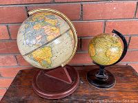 Two vintage tin globes displayed side by side showing size difference and metal stands.