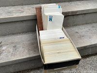 Large cardboard box filled with numerous first day covers and a brown stamp souvenir album.