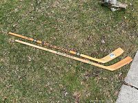 Two wooden Sher-Wood hockey sticks laid on grass, showing full length of sticks and branding.