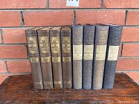 Front view of 8 books arranged side by side with spines facing front: 4 volumes of "The Story of Architecture" in brown and 4 volumes of "The History of Modern Art" in blue/gray.