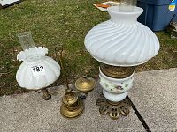 Photo showing two vintage oil lamps with white glass shades and brass bases placed outdoors on concrete.