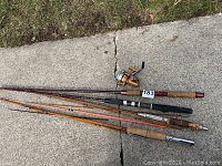 Four fishing rods laid out on concrete, visible cork handles and different shaft materials.