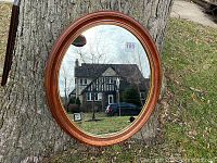 Round wooden framed mirror leaning against a tree outside, showing reflective surface and part of the frame