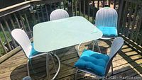 Full set of square table with striped glass top, four chairs and four cushions on deck