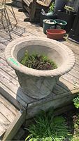 Large concrete planter with woven pattern and soil residue on wood deck