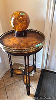 Full view of the round wooden foyer table showing brass trim, legs, and amber glass ornament on top.