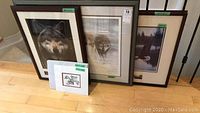 Three framed prints leaning against wall: one wolf face, one double wolf scene, one forest scene
