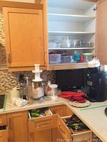 Overview of kitchen counter with Toshiba TV, coffee maker, juicers, oven mitts, and food storage containers in an open cabinet.