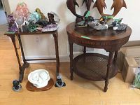 View of two wood occasional tables with various decorative items on and around them. The round table has a cane shelf and leather inlay top, the rectangular table has straight legs and a flat top.