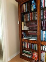 Full wooden bookshelf showing multiple shelves of hardcover books, magazines and DVDs