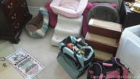 Overview photo showing various small fabric pet beds, fabric-covered pet stairs, a pink round cushion bed, and two fabric soft-sided carry bags in teal and pink.