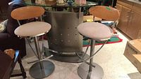 Contemporary bar with two adjustable bar stools in front, showcasing metal bases, wooden backs, and cushioned seats.