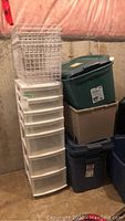 Full view of the plastic drawer storage unit, wire baskets on top, and multiple tote bins stacked adjacent.