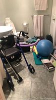 Blue Hugo rollator walker with seat and backrest, blue rollator walker with two wheels and seat, canes, Pilates and fitness equipment including blue exercise ball, foam tubes, yoga mat, white towels hanging on racks in bathroom