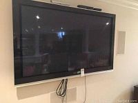 Front view of 57-inch Hitachi flat-screen television mounted on wall with visible cables
