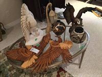 View of the two hand-carved wooden eagle plaques, two pottery pieces, ceramic bald eagle figurine, swan stone lantern, and plaster duck wall sconce arranged on glass-topped table.
