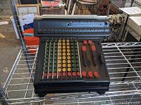 Full front view of the antique Marchant adding machine showing colorful keys, numeric counters, and metal levers on a metal shelf
