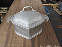 Front angled view of the hammered aluminum triangular Dutch oven showing loop-handled lid and base