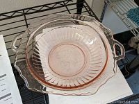 Pink Depression glass fruit bowl shown from a top angle illustrating two open handles, ribbed interior, and decorative molded grape pattern central medallion.