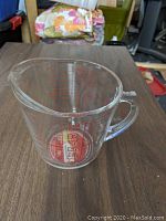 Clear glass Pyrex measuring cup showing full cup and ounce markings with sturdy handle and pouring spout on wooden surface.
