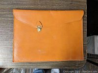 Front view of vintage leather document case with brass clasp on wooden surface.