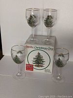Four Spode Christmas Tree all-purpose wine glasses placed on and around the original box, showing the glassware and design details.