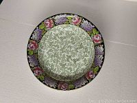 Top view of the bowl showing the floral border with pink roses and purple flowers on a dark background, with green dense foliage pattern in the center.