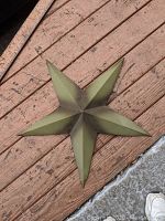 Top-down view of the six-point green painted tin star showing 3D facets and surface texture on outdoor wooden deck.