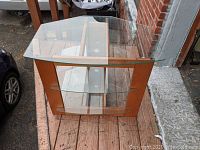 Front view of glass and wood TV stand on wooden deck showing two glass shelves and wood frame structure.