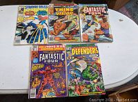 Wide shot of all five comics showing front covers laid flat on a white table: Strange Tales #1, Marvel Two in One #39, Fantastic Four #93, Fantastic Four #147, Defenders #29