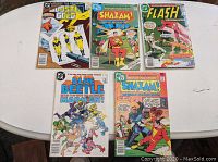 Five DC Comics Bronze Age comic books displayed on a white table showing titles Flash #266, Shazam! #31 & #32, Blue Beetle #3 and Booster Gold #6 with colorful covers.