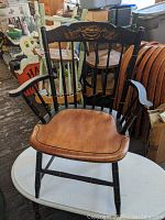 Front view of Hitchcock chair showing black painted frame and natural wood contoured seat with floral stenciling on top rail of backrest.