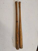Two vintage wooden baseball bats laid side by side, showing one with Boston Red Sox logo and wear on both bats.