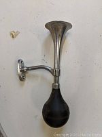 Full view of vintage chrome car horn with black rubber bulb and wall mount bracket.