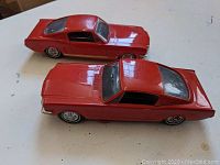 Two red Philco P-22 Ford Mustang model radios side by side on a white surface, visible details of body and wheels.