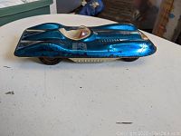 Side view of vintage blue sports car toy showing paint wear, windscreen, and white seat insert.