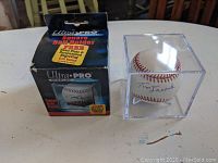 Official autographed baseball in clear display case beside original box on table.