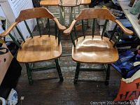 Pair of captain's chairs made of maple wood with natural finish seats and green painted legs and spindles on wooden floor.