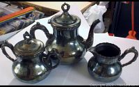 Three piece quadruple plate tea set with teapot, sugar bowl and creamer, detailed view showing tarnished silver finish and ornate design