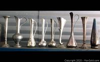 All 9 silverplate bud vases and ewers in a row on shelf
