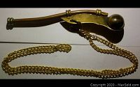 Full view of boatswain's whistle lying flat with attached brass chain