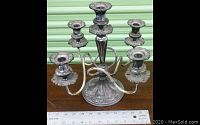Full view of the 5-arm silverplated candelabra with each arm curved outward and floral collars on candle holders, placed next to a ruler for scale.
