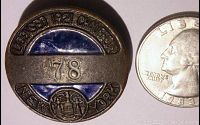 Front view of the 1920/21 New York Chauffeur License Badge with visible text, number 78, blue enamel, and state emblem, next to a quarter for size reference.