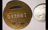 Front side of the badge showing 'Licensed Chauffeur New York', serial number 542667, expiring July 1, 1927, with a quarter coin for size comparison.