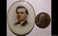 Front view of oval glass portrait with silver metal rim alongside a quarter for scale.