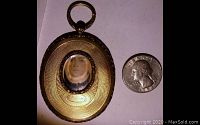 Close-up of vintage silver-tone oval locket with beveled glass window showing miniature portrait and size comparison with quarter coin.