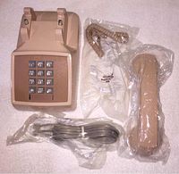 Vintage Western Electric phone body with keypad, handset, coiled cord, and long cord in plastic packaging laid out for display